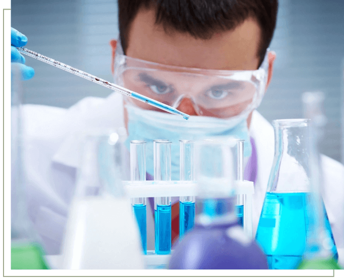 A man in lab coat and goggles looking at blue liquid.